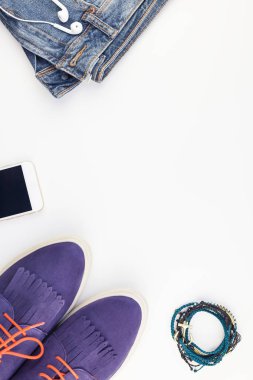 Düz beyaz arka plan kopya alanı ile kulaklıktan süet ayakkabı, kot, bilezik ve smartphone yatırın. Kadın rahat kıyafet havai görünümü. Trendy hipster bak üstten görünüm