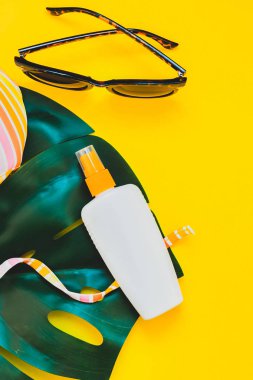 Tropikal orman palm monstera bırakır, güneş gözlüğü, güneş kremi boş şişe mockup ve kadının mayo üst parlak sarı kağıt arka plan üzerinde. Metin için yaratıcı düz yatıyordu kavramı şablon yaz tatil