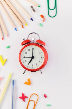 Çalar saat, renk okulu ve ofis malzemelerini kopya alanı, çerçeve, metin veya tasarım şablonu olan beyaz masa arkaplanına yerleştirerek okul kavramına yaslan