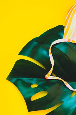 Tropikal orman palmiye monstera yaprakları ve bir kadının mayo üstüne parlak sarı kağıt arka plan. Metin için yaratıcı düz yatıyordu kavramı şablon yaz tatil