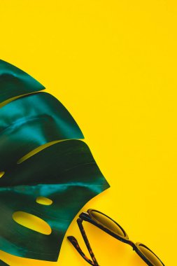 Tropikal orman palm monstera yaprakları, parlak sarı Kağıt arka plan üzerinde güneş gözlüğü. Metin için yaratıcı düz yatıyordu kavramı şablon yaz tatil