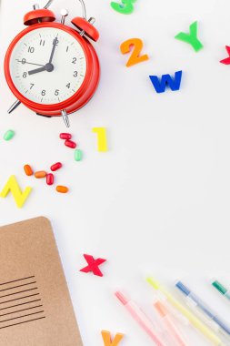 Çalar saat, renk okulu ve ofis malzemelerini kopya alanı, çerçeve, metin veya tasarım şablonu olan beyaz masa arkaplanına yerleştirerek okul kavramına yaslan