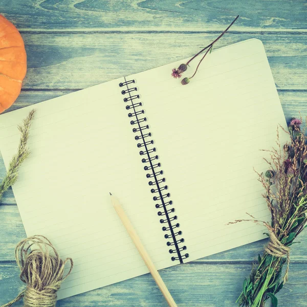 Square Top view of autumn orange pumpkins and dry flowers with grass thanksgiving background over blue toned wooden table with notebook mock up and copy space in rustic style, template for text