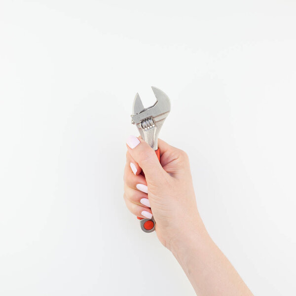 Creative square image of woman hand with pastel manicure polish holding spanner with copy space isolated on white background in minimalism style. Repair or improvement feminism concept