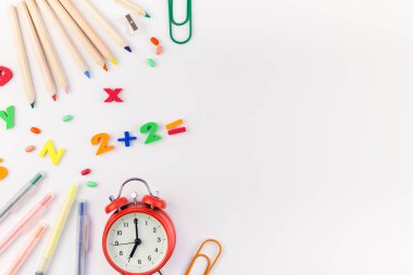 Çalar saat, renk okulu ve ofis malzemelerini kopya alanı, çerçeve, metin veya tasarım şablonu olan beyaz masa arkaplanına yerleştirerek okul kavramına yaslan