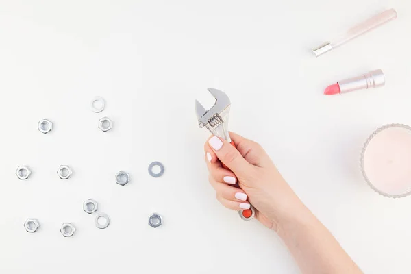 Creative image of woman hand with pastel manicure polish holding spanner with copy space nuts and cosmetics isolated white background in minimalism style. Repair or improvement feminism concept