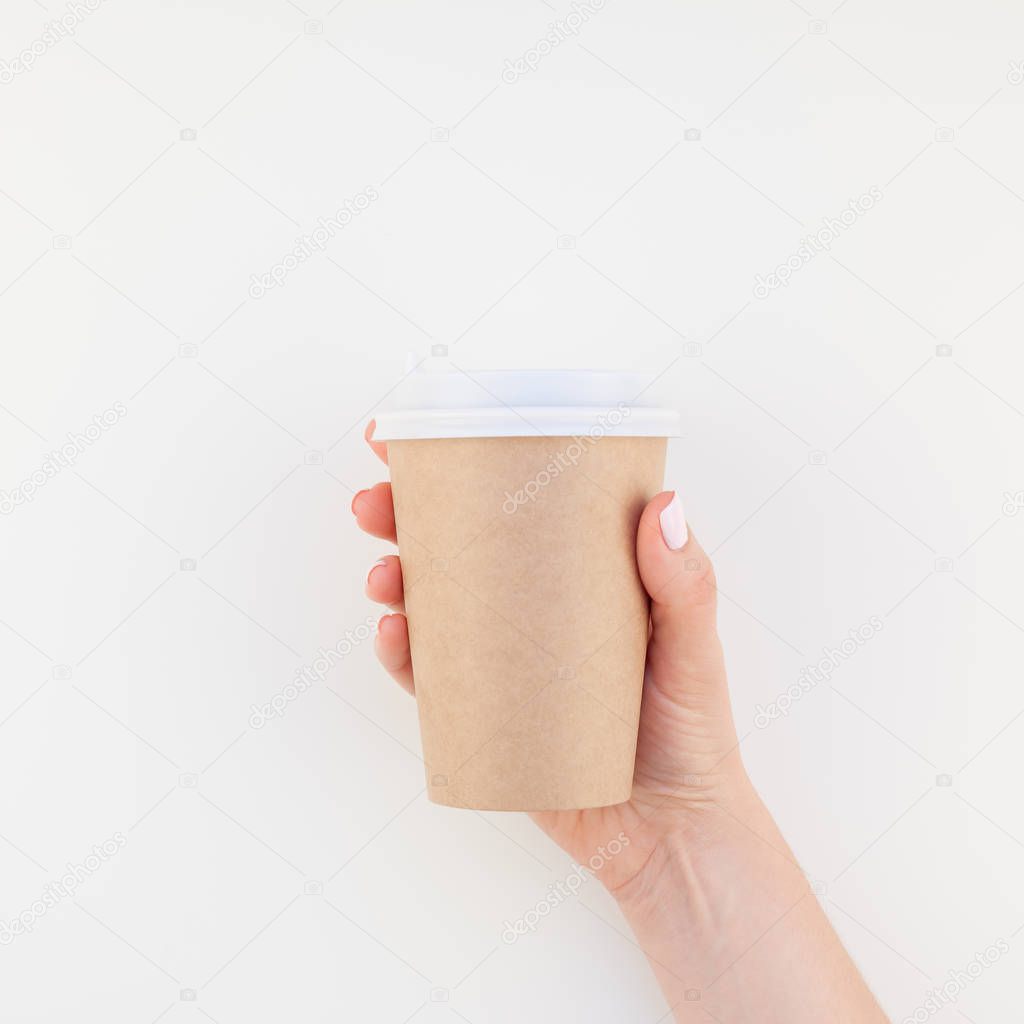 Square mock up image of woman hand holding craft paper coffee cup with copy space isolated on white background in minimalism style. Template for feminine blog, social media