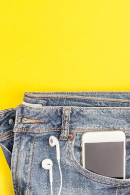 Düz mavi kot pantolon ve smartphone kalın sarı Kağıt arka plan kopya alanı ile kulaklıktan yatırın. Kadın rahat kıyafet havai görünümü. Trendy hipster bak üstten görünüm