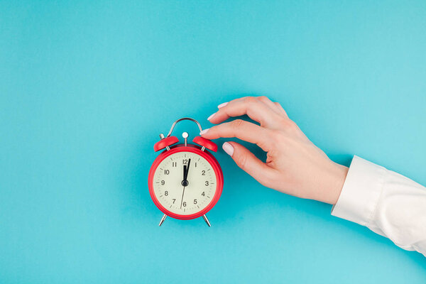 Креативный плоский вид сверху на женщину в белой рубашке с красным винтажным будильником на ярко-синем бирюзовом бумажном фоне с копировальным пространством в минимальном стиле, искушающим текст
