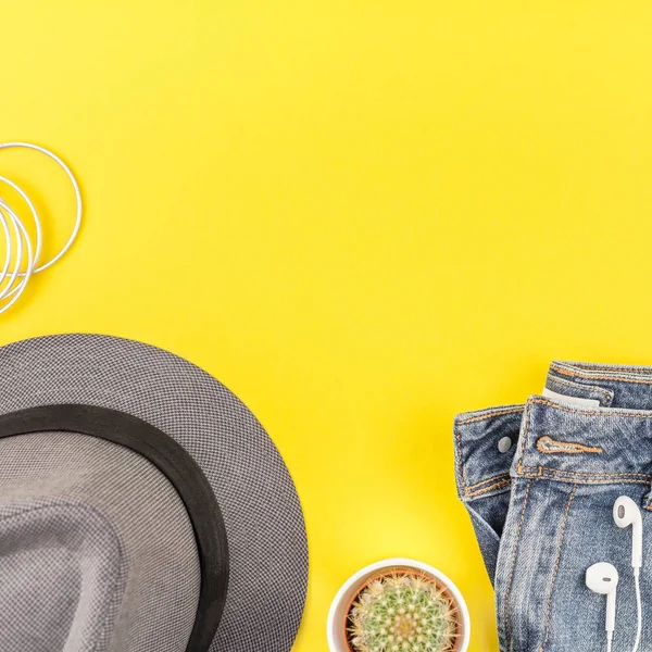 Düz mavi jeans, gri şapka, kaktüs ve akıllı telefon kulaklık kalın sarı Kağıt arka plan üzerinde kopya alanı ile yatıyordu. Kadın rahat kıyafet havai görünümü. Kare hipster bak üstten görünüm