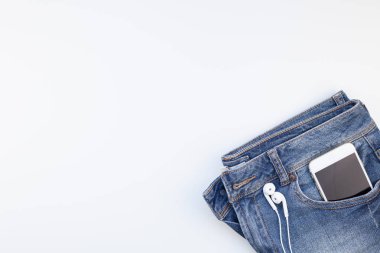 Düz mavi kot pantolon ve beyaz arka plan kopya alanı ile izole smartphone kulaklık yatıyordu. Kadın rahat kıyafet havai görünümü. Trendy hipster bak üstten görünüm