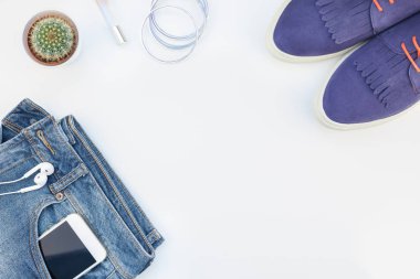 Düz beyaz arka plan kopya alanı ile kulaklıktan süet ayakkabı, kot, bilezik ve smartphone yatırın. Kadın rahat kıyafet havai görünümü. Trendy hipster bak üstten görünüm