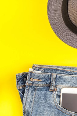 Düz mavi jeans, gri şapka ve akıllı telefon kulaklık kalın sarı Kağıt arka plan üzerinde kopya alanı ile yatıyordu. Kadın rahat kıyafet havai görünümü. Trendy hipster bak üstten görünüm