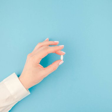 En az tarzı, kare şablon metin için kopya alanı pastel kağıt mavi zemin üzerine beyaz bir hap tutan kadın el. Tıbbi tedavi, eczane, sağlık kavramı