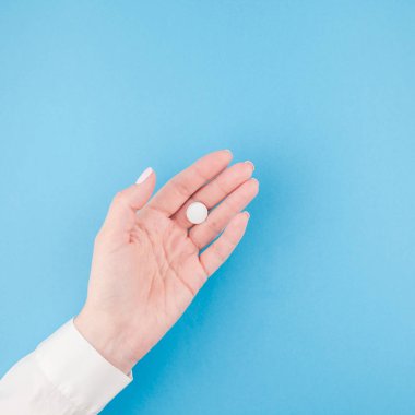 En az tarzı, kare şablon metin için kopya alanı pastel kağıt mavi zemin üzerine beyaz bir hap tutan kadın el. Tıbbi tedavi, eczane, sağlık kavramı