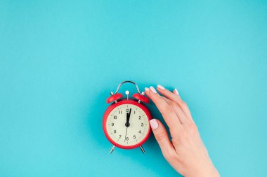 Yaratıcı düz yatıyordu kavramı kırmızı vintage çalar saat parlak mavi turkuaz üzerinde tutan kadın el üst görünümünü renk Kağıt arka plan kopya alanı ile en az tarzı, metin için şablon
