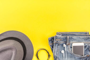 Düz mavi jeans, gri şapka ve akıllı telefon kulaklık kalın sarı Kağıt arka plan üzerinde kopya alanı ile yatıyordu. Kadın rahat kıyafet havai görünümü. Trendy hipster bak üstten görünüm