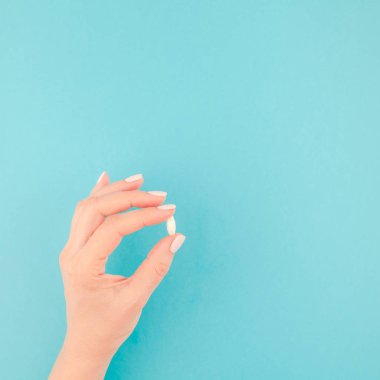 En az tarzı, kare şablon metin için kopya alanı pastel kağıt mavi zemin üzerine beyaz bir hap tutan kadın el. Tıbbi tedavi, eczane, sağlık kavramı