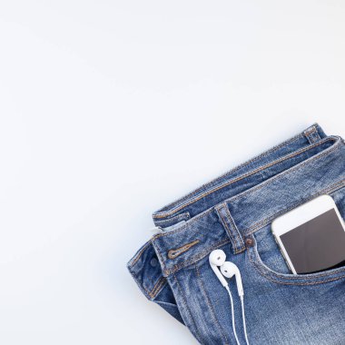 Kare düz mavi kot pantolon ve beyaz arka plan kopya alanı ile izole smartphone kulaklık yatıyordu. Kadın rahat kıyafet havai görünümü. Trendy hipster bak üstten görünüm