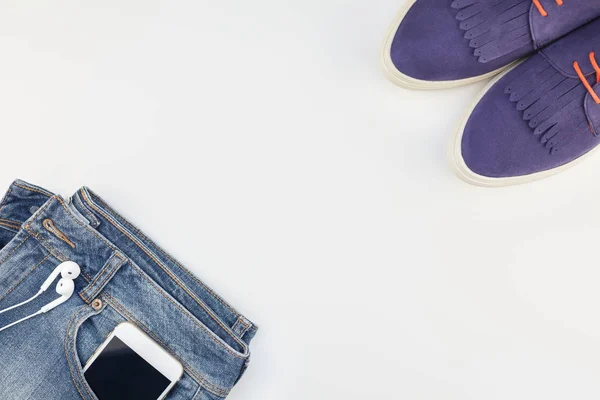 平躺的麂皮绒鞋 蓝色牛仔裤和智能手机与耳机在白色背景与复制空间 女性休闲服装的头顶景色 时髦的时髦的看顶部视图 — 图库照片