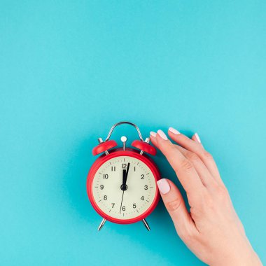 Yaratıcı düz yatıyordu kavramı kırmızı vintage çalar saat üzerinde kare parlak mavi turkuaz tutan kadın el üst görünümünü renk Kağıt arka plan kopya alanı ile en az tarzı, metin için şablon