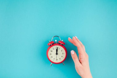 Yaratıcı düz yatıyordu kavramı kırmızı vintage çalar saat parlak mavi turkuaz üzerinde tutan kadın el üst görünümünü renk Kağıt arka plan kopya alanı ile en az tarzı, metin için şablon