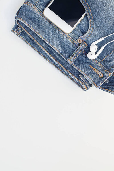 Flat lay of suede shoes, blue jeans and smartphone with headphones on white background with copy space. Overhead view of woman casual outfit. Trendy hipster look top view