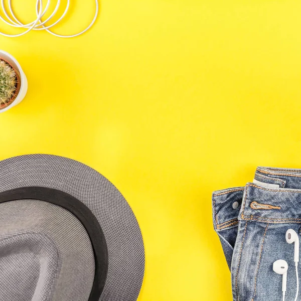 Düz mavi jeans, gri şapka, kaktüs ve akıllı telefon kulaklık kalın sarı Kağıt arka plan üzerinde kopya alanı ile yatıyordu. Kadın rahat kıyafet havai görünümü. Kare hipster bak üstten görünüm