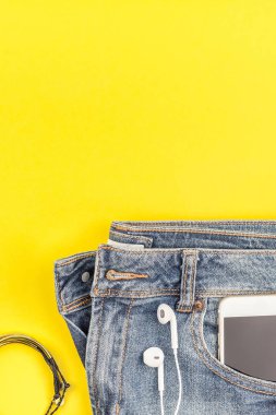 Düz mavi kot pantolon ve smartphone kalın sarı Kağıt arka plan kopya alanı ile kulaklıktan yatırın. Kadın rahat kıyafet havai görünümü. Trendy hipster bak üstten görünüm