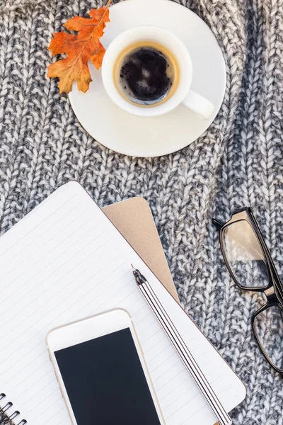 Creative autumn flat lay overhead top view stylish home workspace with smartphone notebook coffee cup cozy gray knitted plaid background copy space. Fall season template for feminine blog social media