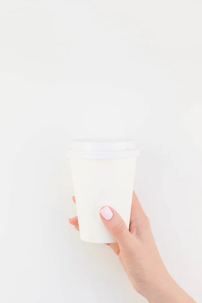 Creative mock up image of woman hand holding paper coffee cup with copy space isolated on white background in minimalism style. Template for feminine blog, social media