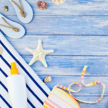 Kare yaratıcı düz yaz seyahat tatil kavramı yatıyordu. Plaj havlu güneş kremi şişe mayo deniz kabuklarını denizyıldızı pastel mavi ahşap plakalar arka plan kopya alanı mockup şablon metin üstten görünüm