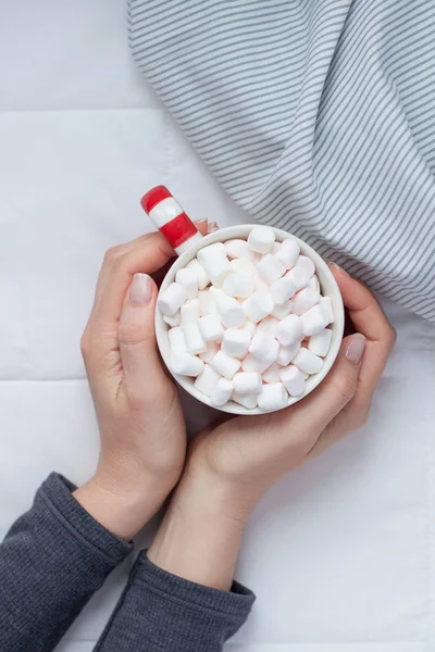 New Year or Christmas flat lay top view with Hot cacao coffee chocolate with marshmallows mug in woman hands Xmas holiday celebration in bed with lights. Concept blog social media 2019