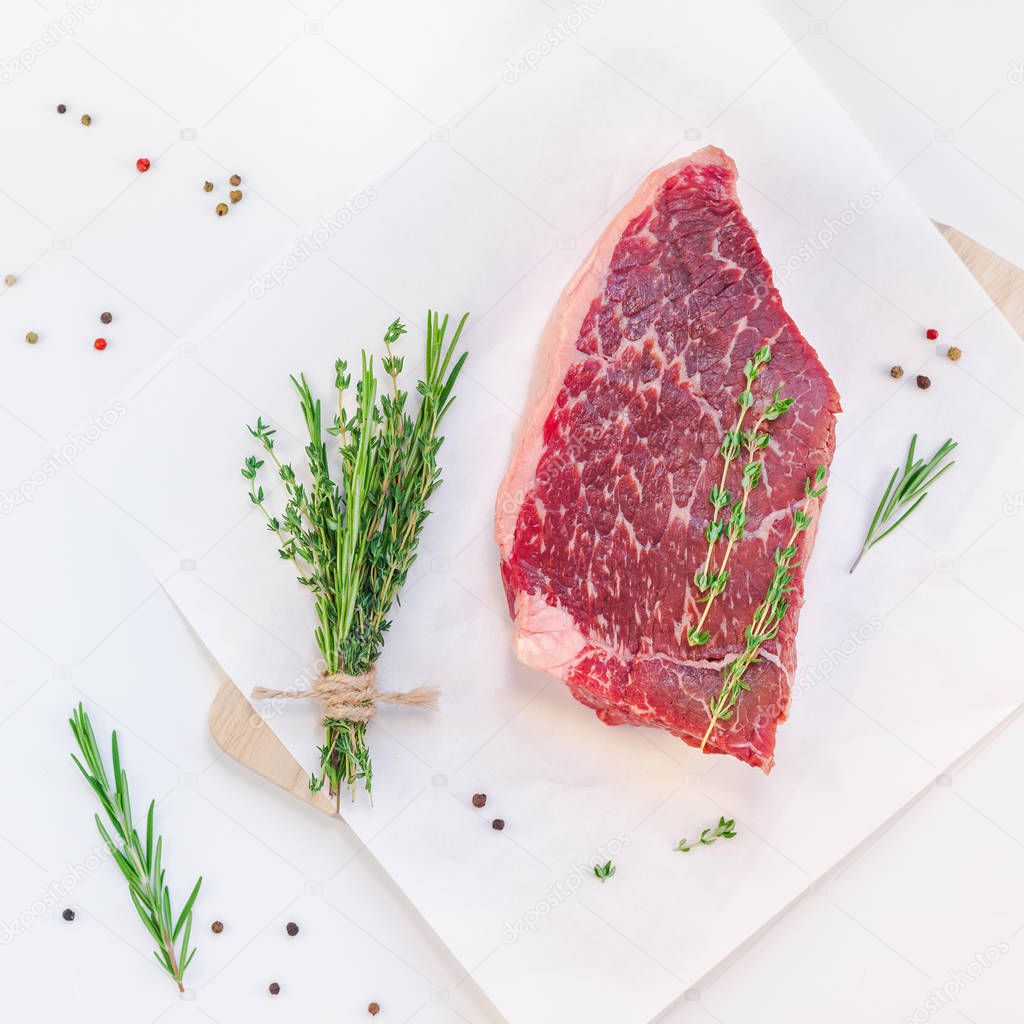 Creative Top view flat lay of fresh raw beef meat striploin steak with rosemary thyme herbs garlic pepper mushrooms on white background with copy space. Food preparation cooking Square concept