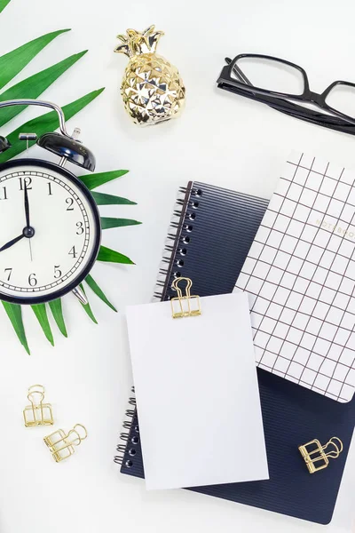 Top view flat lay office workspace desk styled design office supplies alarm clock tropical palm leaves smartphone camera copy space black white background. Template office feminine blog social media