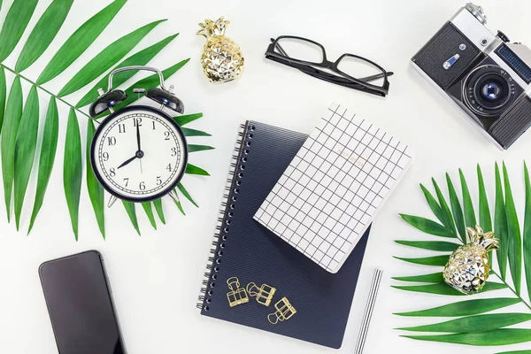 Top view flat lay office workspace desk styled design office supplies alarm clock tropical palm leaves smartphone camera copy space black white background. Template office feminine blog social media