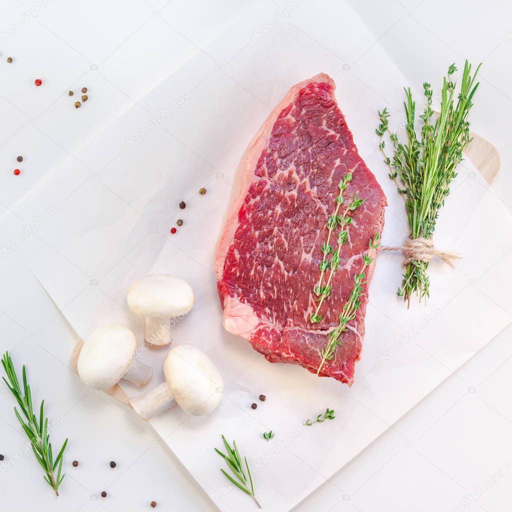 Creative Top view flat lay of fresh raw beef meat striploin steak with rosemary thyme herbs garlic pepper mushrooms on white background with copy space. Food preparation cooking Square concept
