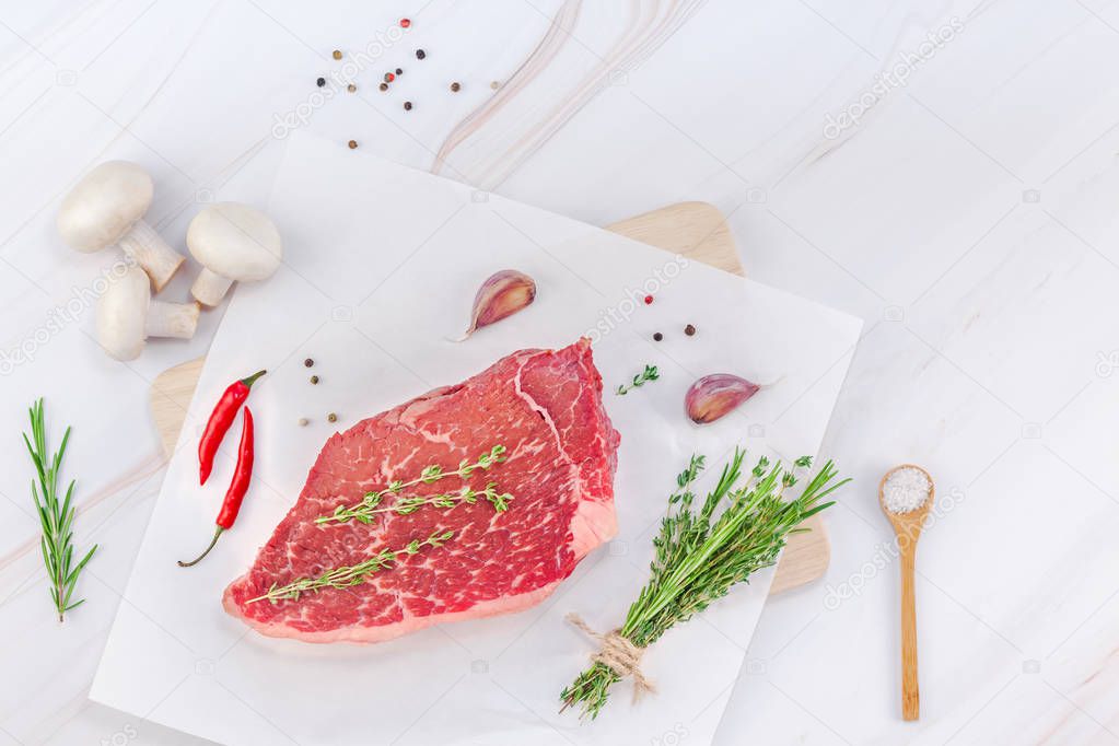 Creative Top view flat lay of fresh raw beef meat striploin steak rosemary thyme herbs garlic meat pepper mushrooms white marble table background with copy space. Food meat preparation cooking concept