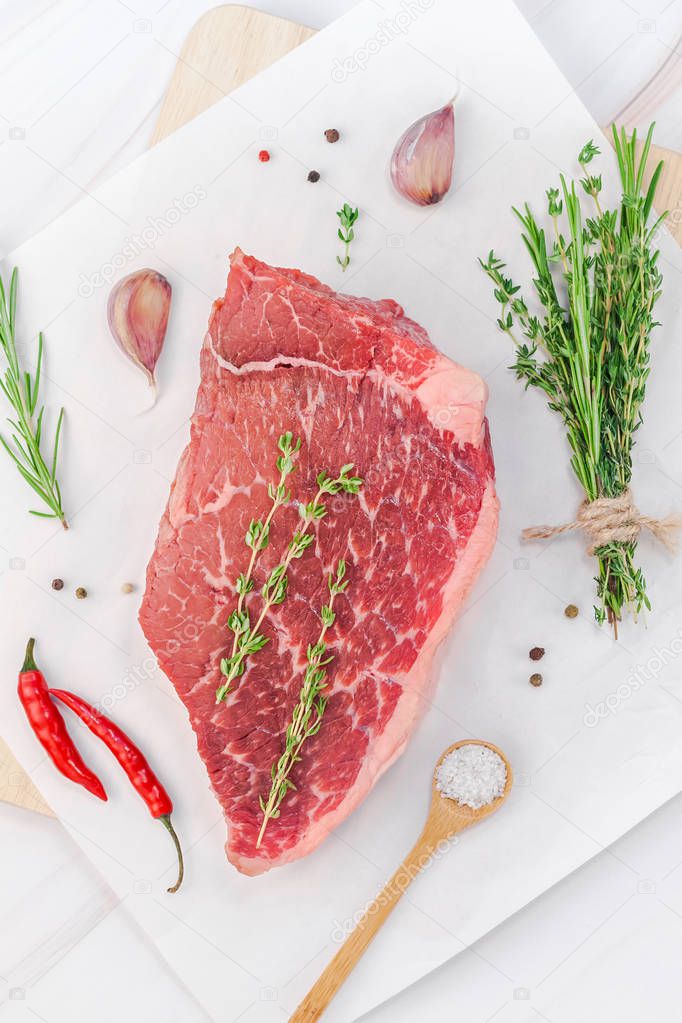 Creative Top view flat lay of fresh raw beef meat striploin steak with rosemary thyme herbs garlic pepper mushrooms on white marble table background with copy space. Food preparation cooking concept