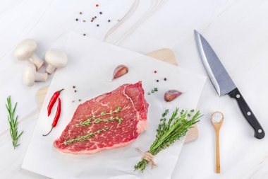 Yaratıcı üstten görünüm taze çiğ sığır eti striploin biftek biberiye kekik otlar sarımsak et biber mantar beyaz mermer masa arka plan kopya alanı ile düz yatıyordu. Gıda et hazırlık pişirme kavramı