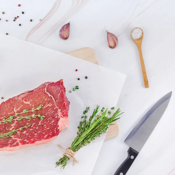 Yaratıcı en iyi görünüm düz yatıyordu taze çiğ sığır eti striploin biftek biberiye kekik otlar sarımsak biber mantar et beyaz mermer masa arka plan kopya alanı. Kare kavramı yemek yiyecek et hazırlama