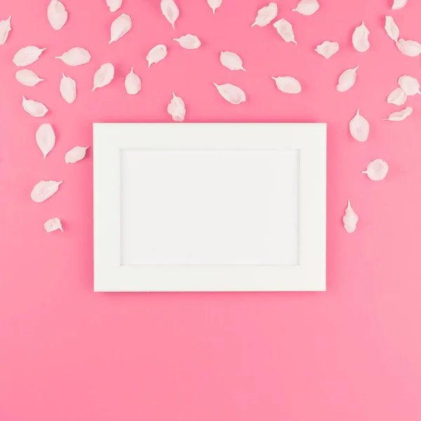 Creative flat lay concept top view of white frame mock up and apple tree flowers petals on square pastel pink background with copy space in minimal style, template for text
