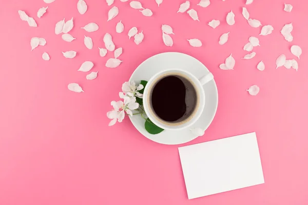 Creative flat lay concept top view of coffee cup and white apple tree flowers petals on pastel pink background with postcard mock up and copy space in minimal style, template for text