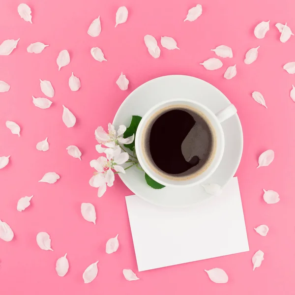 Creative flat lay concept top view of coffee cup and white apple tree flowers petals on pastel pink square background with postcard mock up and copy space in minimal style, template for text