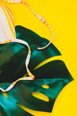 Tropikal orman palmiye monstera yaprakları ve bir kadının mayo üstüne parlak sarı kağıt arka plan. Metin için yaratıcı düz yatıyordu kavramı şablon yaz tatil