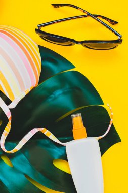 Tropikal orman palm monstera bırakır, güneş gözlüğü, güneş kremi boş şişe mockup ve kadının mayo üst parlak sarı kağıt arka plan üzerinde. Metin için yaratıcı düz yatıyordu kavramı şablon yaz tatil