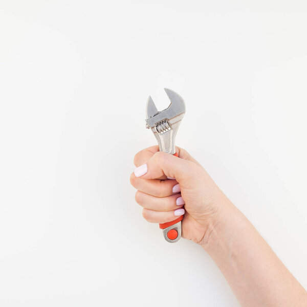 Creative square image of woman hand with pastel manicure polish holding spanner with copy space isolated on white background in minimalism style. Repair or improvement feminism concept