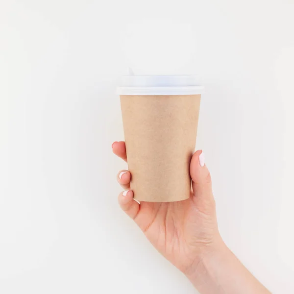 Square mock up image of woman hand holding craft paper coffee cup with copy space isolated on white background in minimalism style. Template for feminine blog, social media