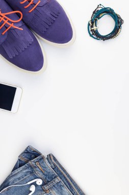 Düz beyaz arka plan kopya alanı ile kulaklıktan süet ayakkabı, kot, bilezik ve smartphone yatırın. Kadın rahat kıyafet havai görünümü. Trendy hipster bak üstten görünüm