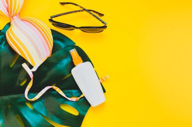 Tropikal orman palm monstera bırakır, güneş gözlüğü, güneş kremi boş şişe mockup ve kadının mayo üst parlak sarı kağıt arka plan üzerinde. Metin için yaratıcı düz yatıyordu kavramı şablon yaz tatil